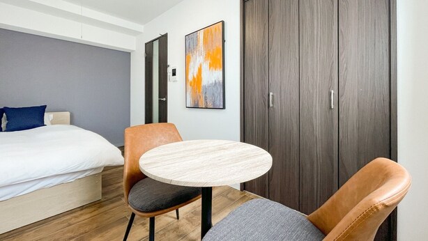 Habitación de hotel con cama, una mesa redonda, dos sillas, un armario y un cuadro en la pared.