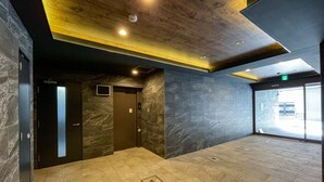 Un interior con un ascensor de tonos oscuros, un techo empotrado con iluminación y una amplia puerta de cristal que da al exterior.