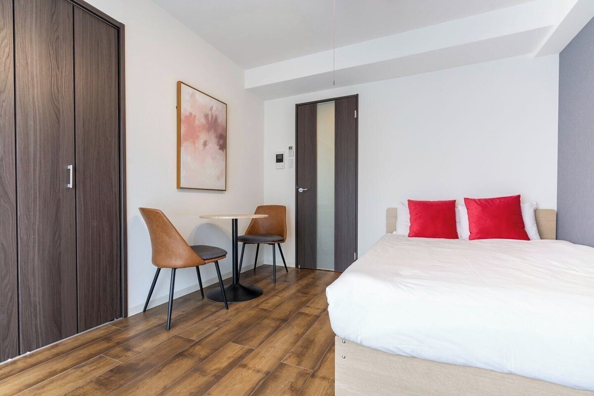 A hotel room with a bed, two chairs, a table, and a door.