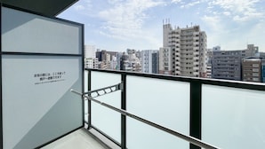 Un balcón con vista a la ciudad, barandilla metálica y puerta de cristal.