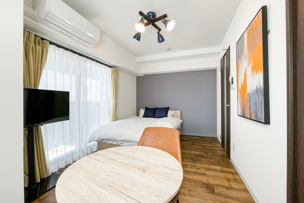 A hotel room with a bed, a TV, a round table, and a painting on the wall.