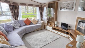 Una sala de estar acogedora con sofá, televisor, chimenea y ventanas amplias.