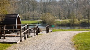 Ein Kiesweg führt zu einer Holzhütte mit Bänken, einem kleinen Schuppen und einem Schild, das auf einen Picknickplatz am See hinweist.