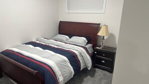 Uma cama bem arrumada com colcha listrada, cabeceira de madeira e mesa de cabeceira com abajur.