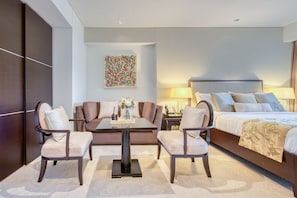 A hotel room with a bed, a sofa, a coffee table, and two armchairs. - Emaar Residences Elegant Studio (Dubai)