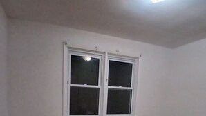 A room with a wooden floor, two windows with white frames, and a ceiling light fixture. -  Lean and cozy home for your family get away (Hamilton)