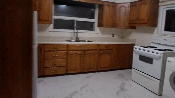 A kitchen with wooden cabinets, a white stove, and a sink. -  Lean and cozy home for your family get away (Hamilton)