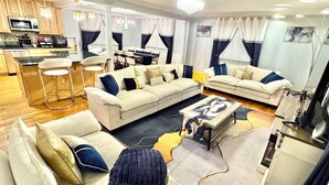A modern living room with a sectional sofa, a coffee table, and a dining area with a bar. - Mid-Term Luxury Family Stay/Hot Tub, 2 Fire Pits, Sauna, Massage Chair & Arcade (Alexandria)