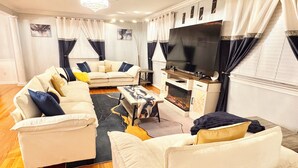 A living room with a sofa set, a flat-screen TV, a fireplace, and a chandelier. - Mid-Term Luxury Family Stay/Hot Tub, 2 Fire Pits, Sauna, Massage Chair & Arcade (Alexandria)