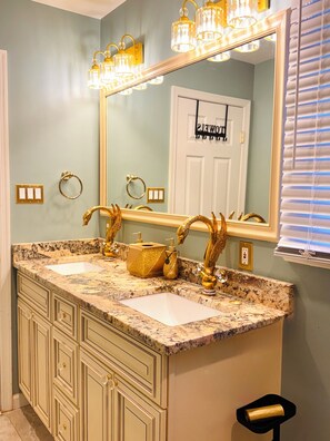 Une salle de bain avec deux lavabos, des robinets dorés, un grand miroir et un meuble-lavabo avec des tiroirs.