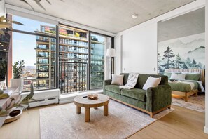 A modern living room with a green sofa, a round wooden coffee table, and a bed with a mountain view mural.