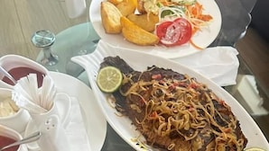A dining table with plates of food, including fried potatoes, a fish dish, and a salad. - Vista Homes Villa (Kigali)
