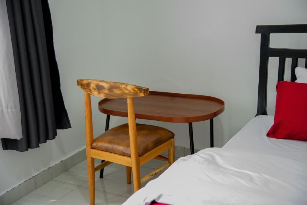 Una habitación con cama, una silla de madera, una mesita y un cojín rojo.