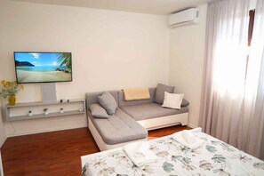 A room with a sofa, a bed with floral bedding, a TV on the wall, and a window with curtains. - Holiday Apartment Castello A2 (Mali Lošinj)
