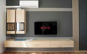Un soggiorno moderno con TV a incasso, mobili contenitori in legno e una panca con riviste.