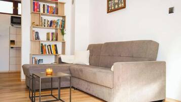 A living room with a grey sofa, a small table with a candle, and a bookshelf filled with books.