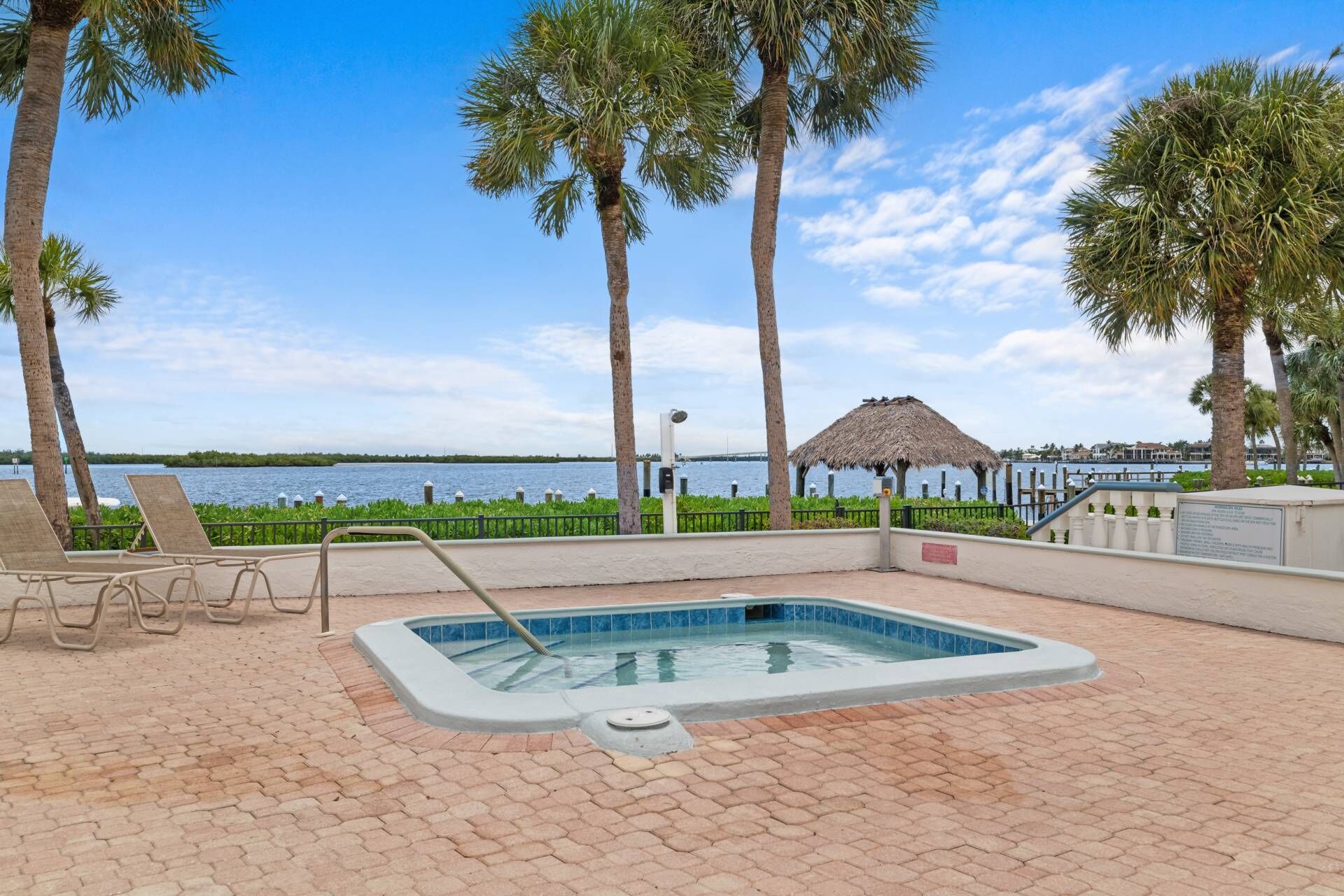 A pool area with lounge chairs, a hot tub, and a view of the water.