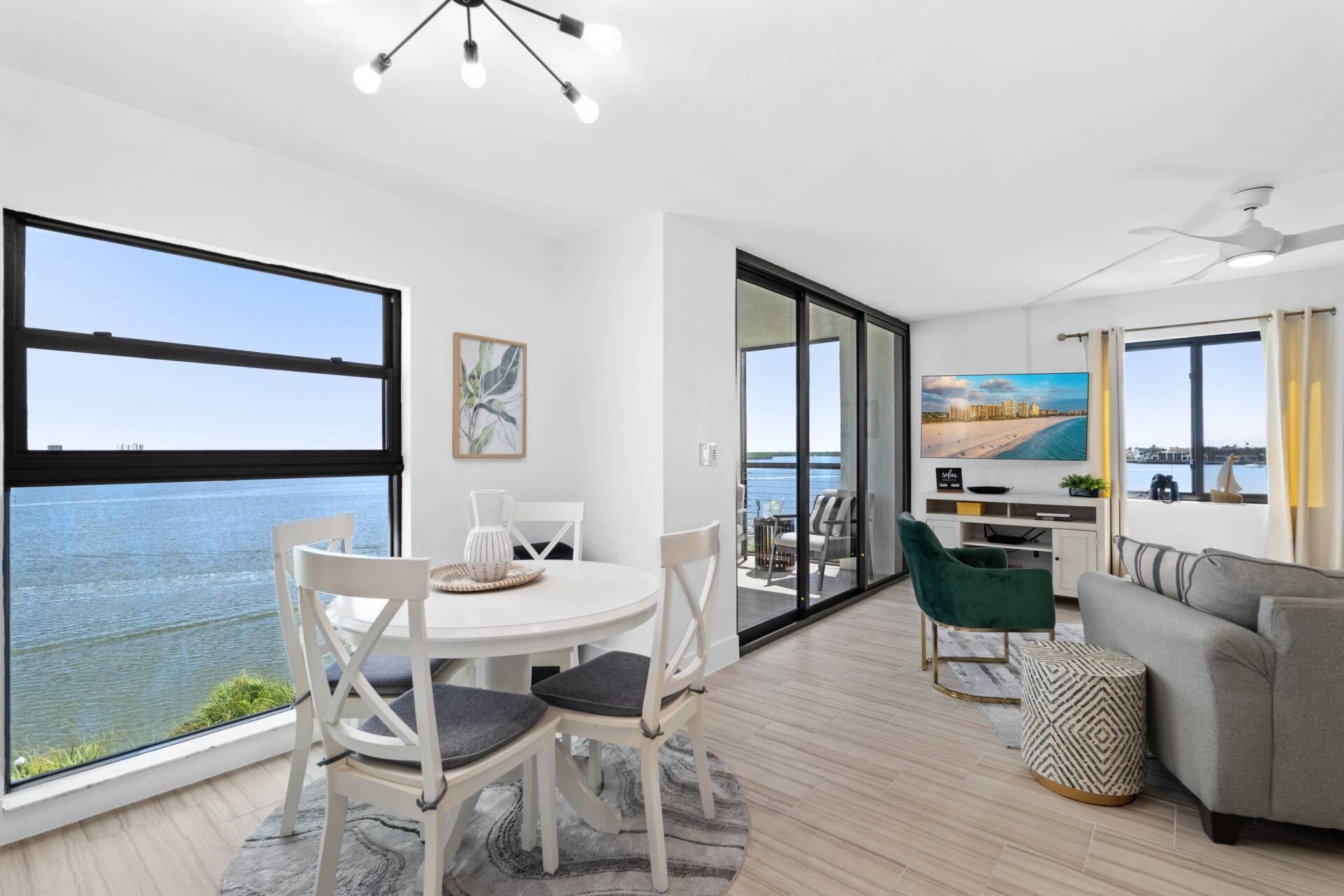 A modern living room with a large window, a dining area with chairs, a sofa, and a TV.