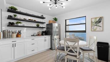 A modern kitchen with white cabinetry, black shelves, and a stainless steel refrigerator.