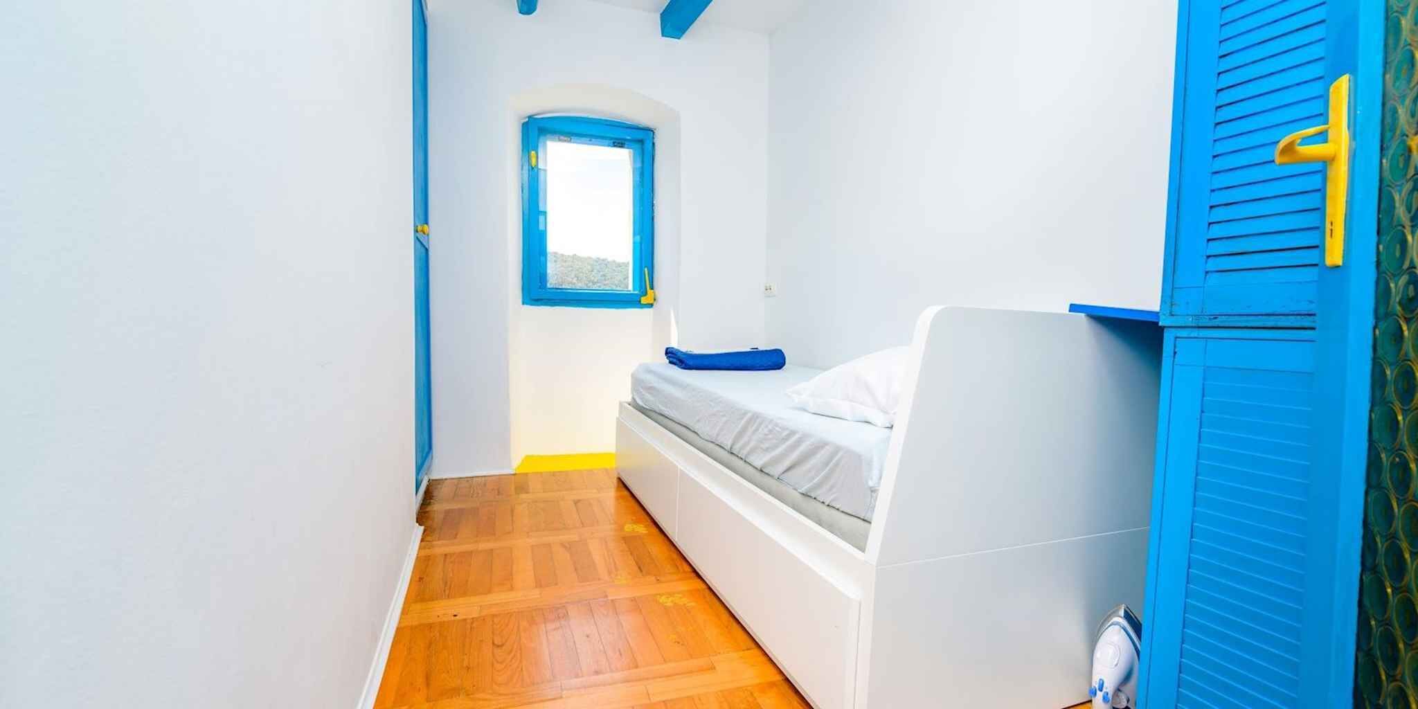 Een kleine kamer met een bed, een raam en een deur.