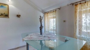 A room with a glass table, a vase with branches, a painting on the wall, and patterned curtains. - Holiday Apartment Biserka B4 B (Cunski)