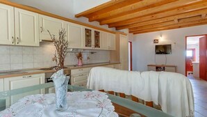 A kitchen with white cabinets, a wooden ceiling, and a dining area with a table covered in a white tablecloth. - Holiday Apartment Biserka B4 B (Cunski)
