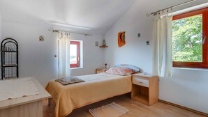 A bedroom with a bed, a nightstand, a window with curtains, a radiator, and a small shelf. - Holiday Apartment Biserka B4 B (Cunski)