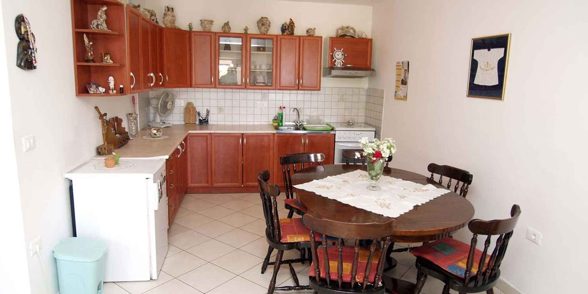 A kitchen with wooden cabinets, a white refrigerator, a dining table with chairs, and a tiled floor.