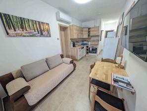 Un espacio habitable compacto con sofá, una mesa de comedor, área de cocina con electrodomésticos modernos y un cuadro en la pared.