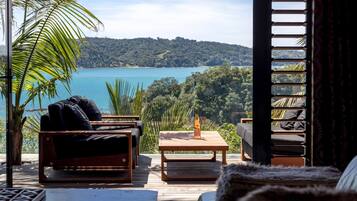 A wooden deck with outdoor furniture, a bottle of wine, and a view of a lake and forest.