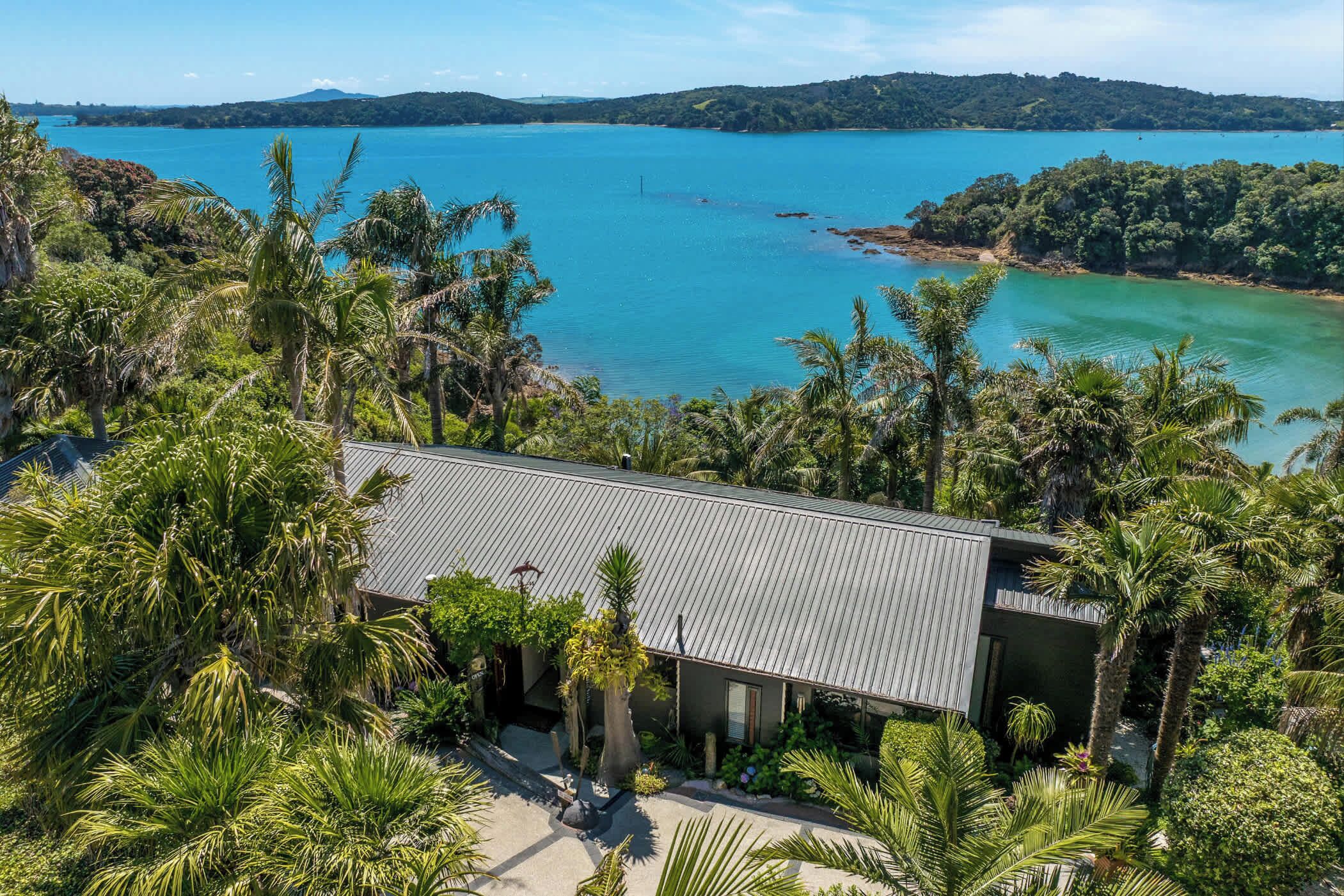 A modern house with a metal roof, surrounded by lush greenery and a view of a large body of water.