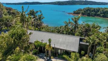 A modern house with a metal roof, surrounded by lush greenery and a view of a large body of water.