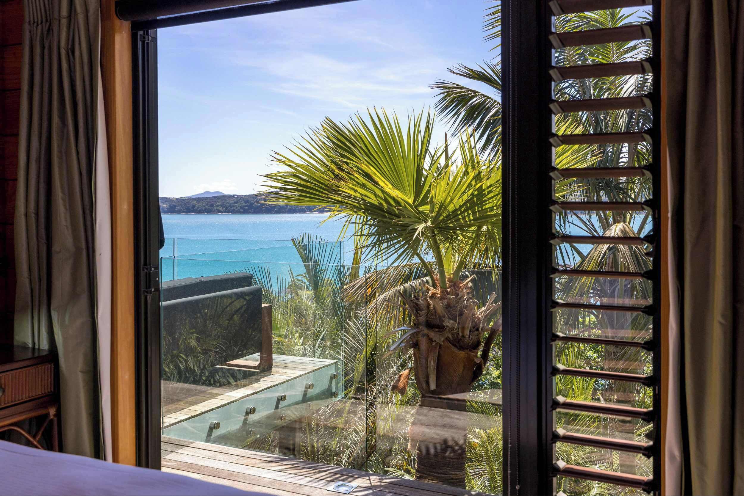 A room with a large window overlooking a body of water, a wooden deck, and a potted plant.