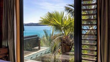 A room with a large window overlooking a body of water, a wooden deck, and a potted plant.