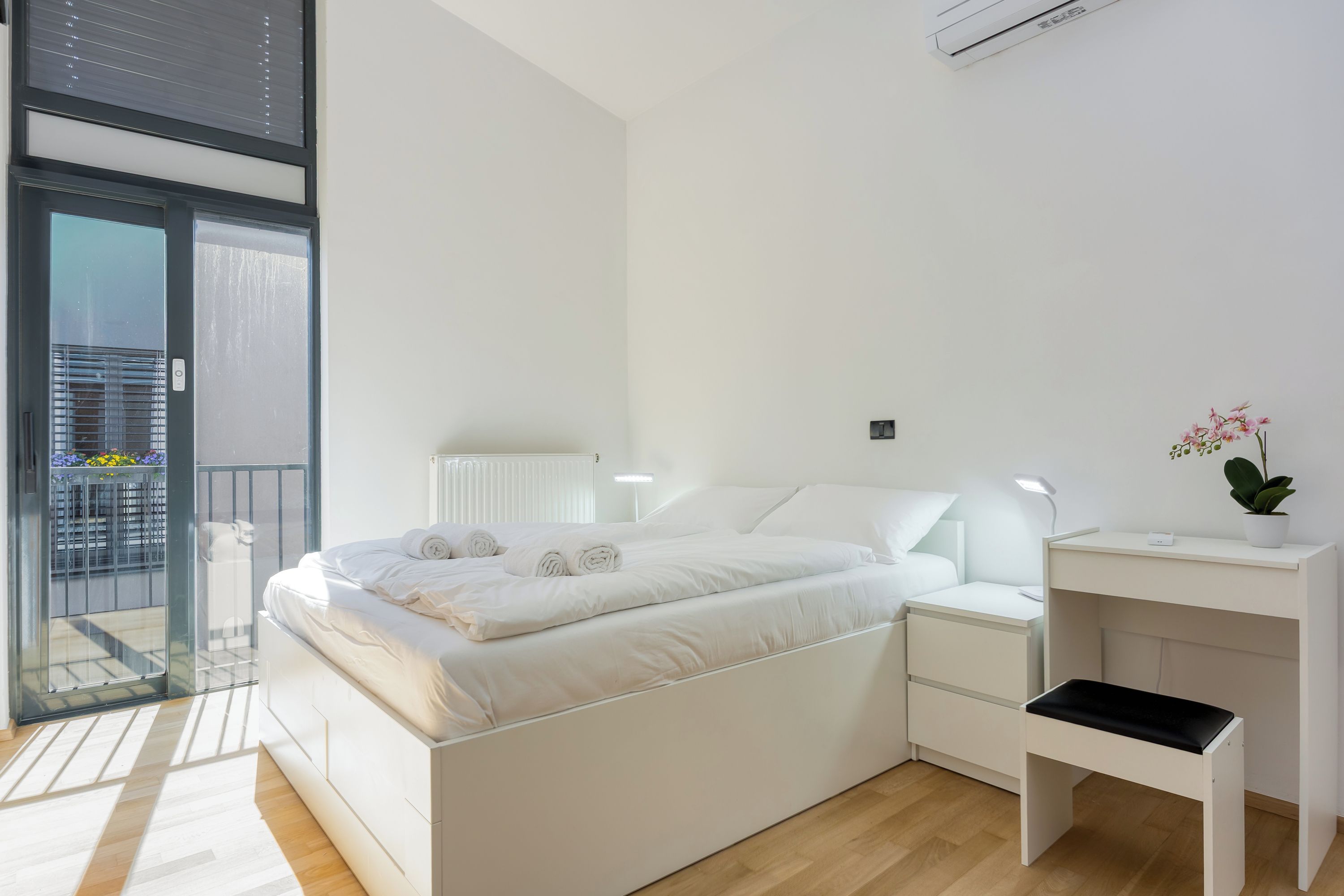 A modern bedroom with a bed, bedside tables, a desk, and a potted plant.