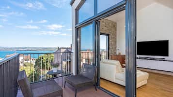 Ein Balkon mit Korbmöbeln, einem Fernseher und Blick aufs Meer.