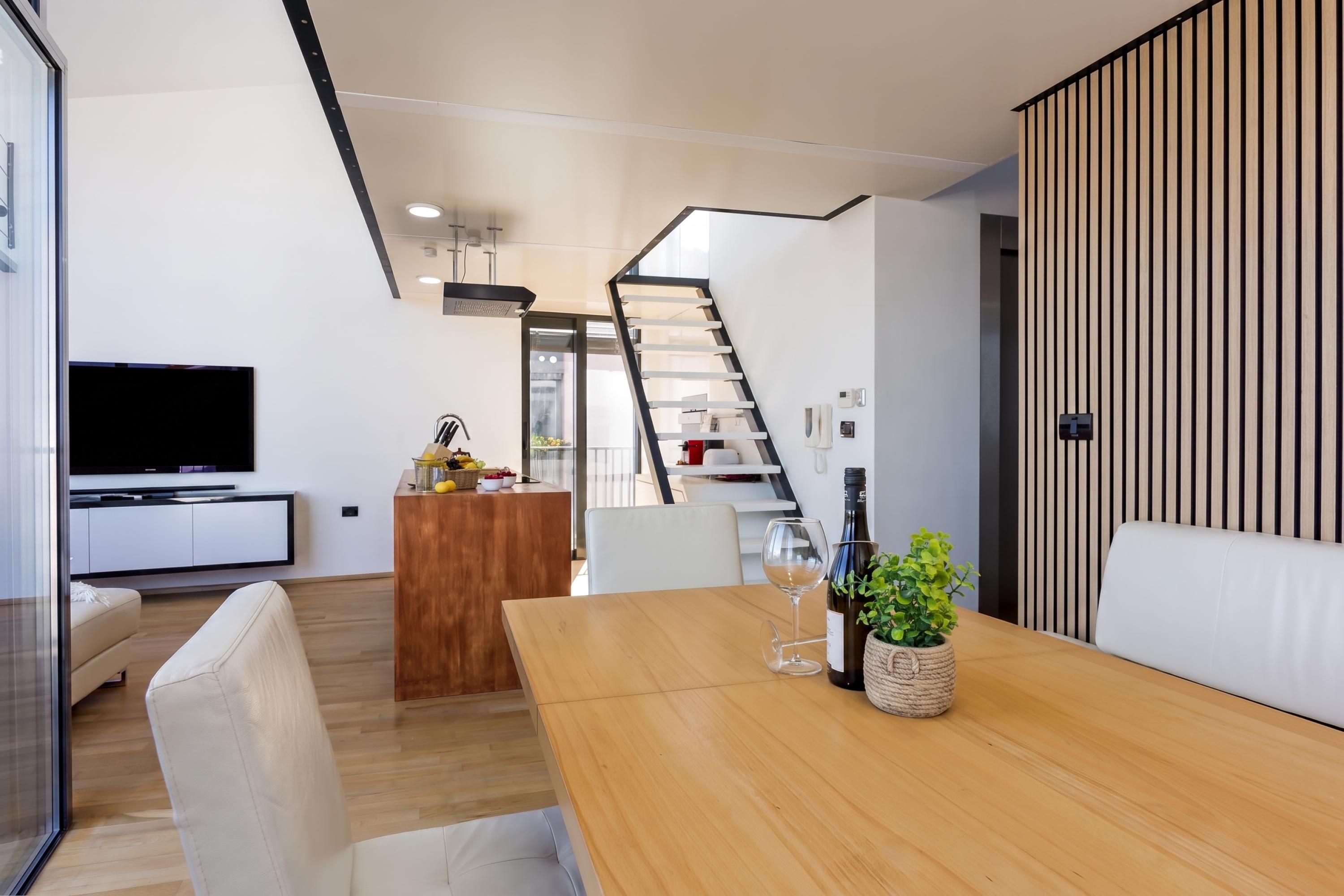 Een moderne woonruimte met een houten eettafel, een televisie en een keuken met een trap.