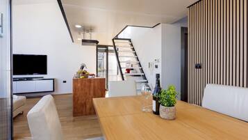 A modern living space with a wooden dining table, a TV, and a kitchen area with a staircase.