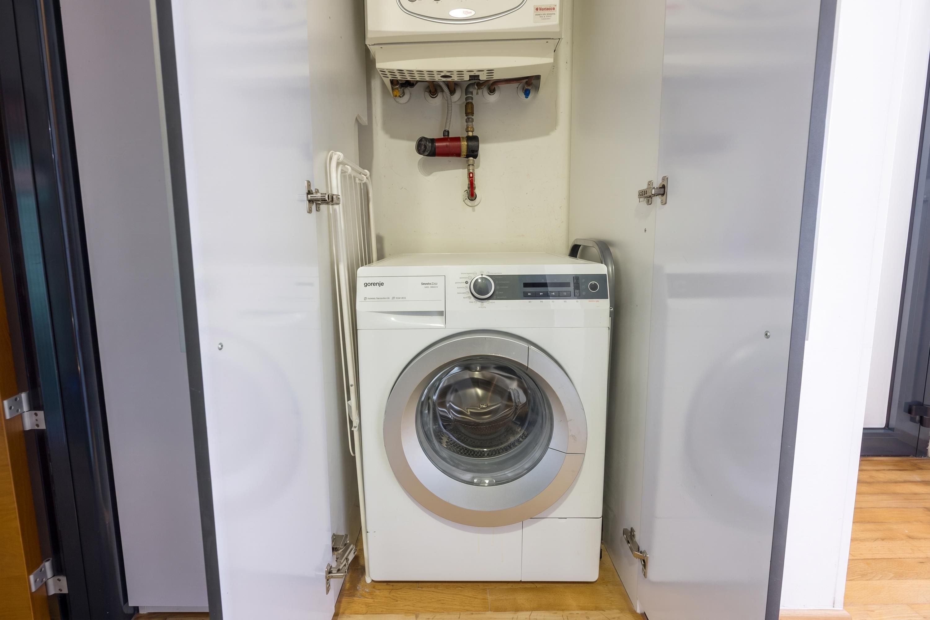 Eine kompakte, weiße Waschmaschine mit Bedienfeld, in einem kleinen, abgeschlossenen Waschraum mit Holzboden.