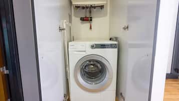 Eine kompakte, weiße Waschmaschine mit Bedienfeld, in einem kleinen, abgeschlossenen Waschraum mit Holzboden.
