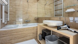 Un bany modern amb banyera, un mirall gran, un lavabo i un assecador de cabells al taulell.