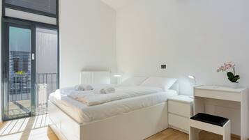 Ein modernes Schlafzimmer mit Bett, Nachttischen, einem Schreibtisch und einer Topfpflanze.