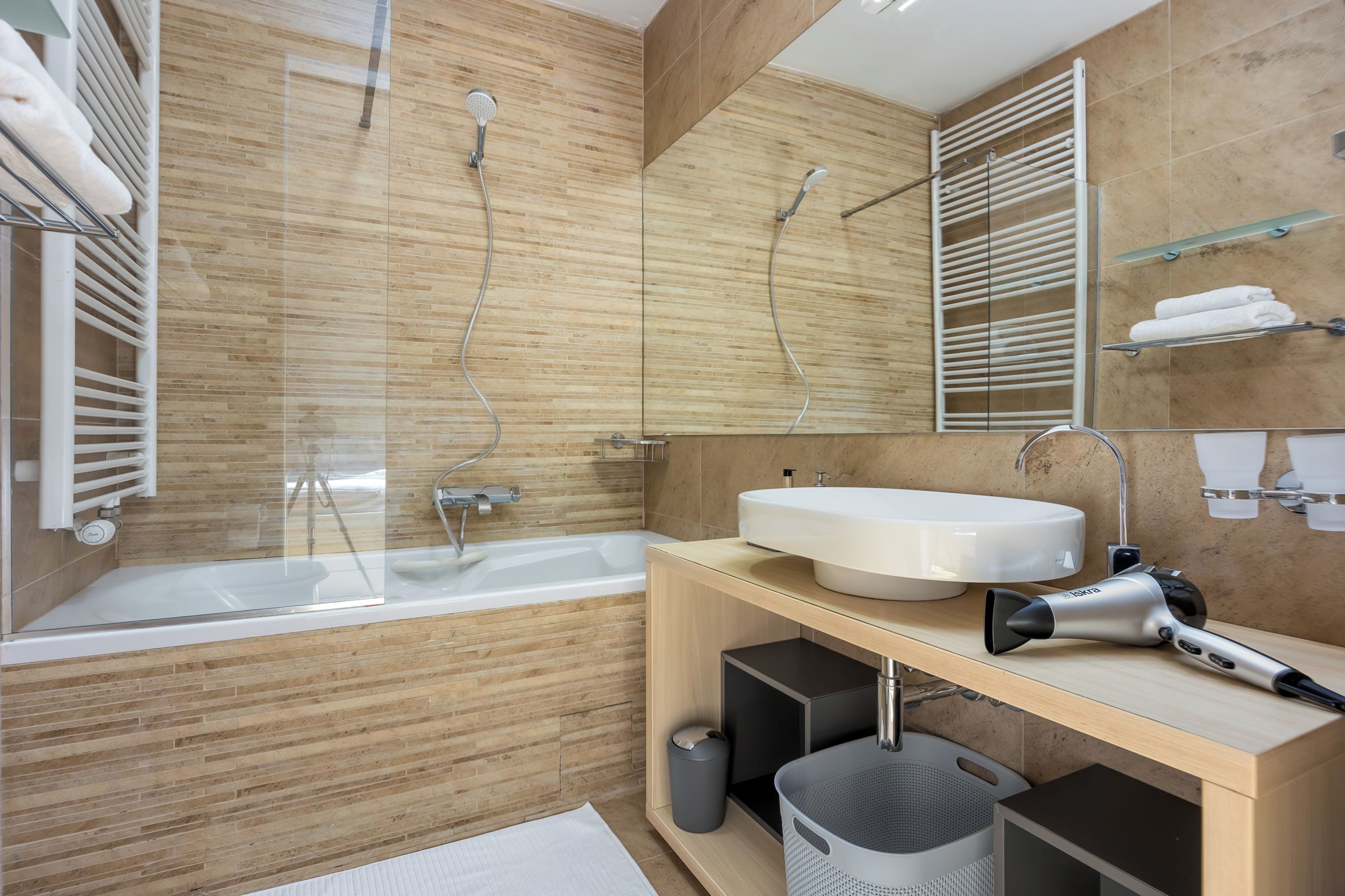 A modern bathroom with a bathtub, a large mirror, a sink, and a hairdryer on the counter.