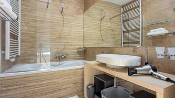 A modern bathroom with a bathtub, a large mirror, a sink, and a hairdryer on the counter.
