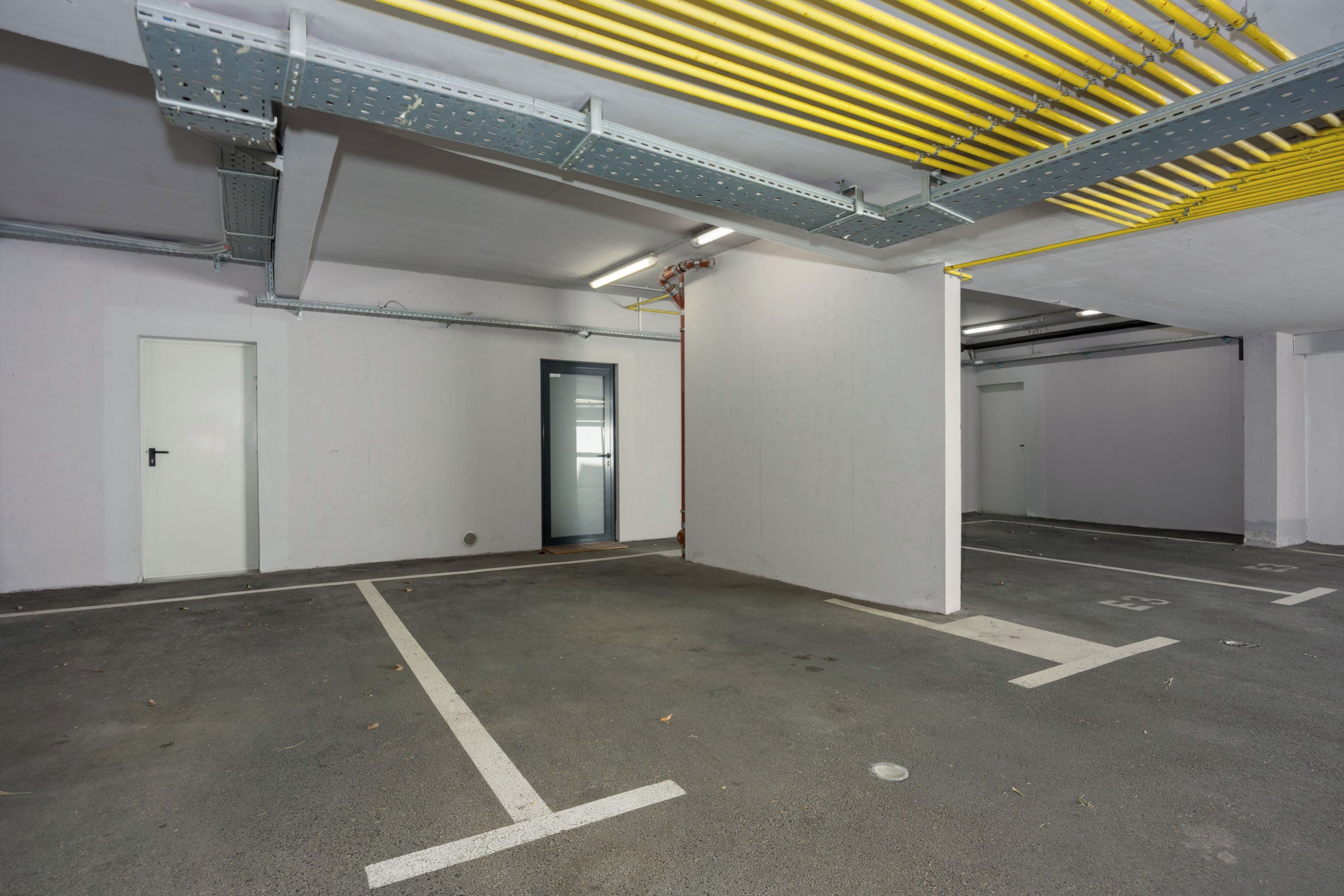 Un parking avec des planchers en béton, des murs blancs et des poutres métalliques.