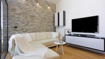 Ein modernes Wohnzimmer mit Steinwand, einem weißen Sofa, einem Flachbildfernseher und einem kleinen Beistelltisch.