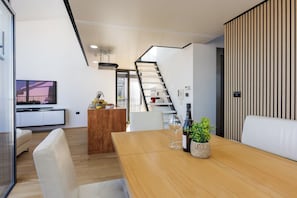 A modern interior with a wooden dining table, white chairs, a kitchen area, and a staircase. - Azure Adriatic Residence w/ Sea-view Balcony (Koper)