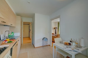 A modern kitchen with a dining area, wooden cabinets, and a small table set for breakfast. - Casa Berna - Balcony Apt With Mountain Views (Lugano)