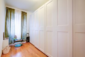 Ein Zimmer mit Holzboden, einem Glastisch mit Büchern und einem Laptop, einem Koffer und einem Korb.