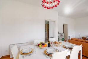 A dining area with a white table set for four, including plates, cutlery, and a bowl of fruit. - Casa Berna - Balcony Apt With Mountain Views (Lugano)